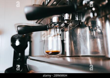 L'espresso fragrante scorre da una macchina per caffè in una tazza. Preparazione di caffè aromatico con attrezzature professionali Foto Stock