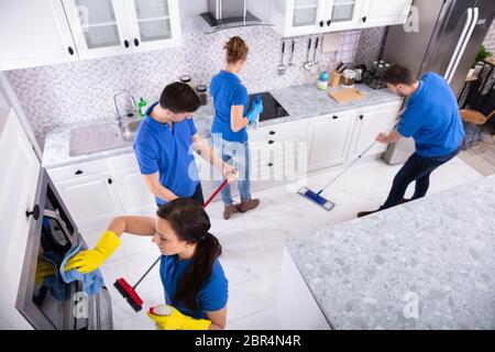 Gruppo di giovani portieri in una pulitura uniforme la cucina di casa Foto Stock