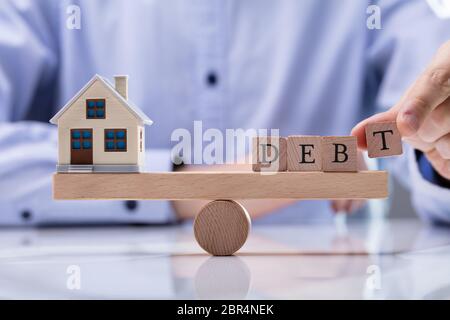 Close-up di imprenditore il canto mettendo il debito di parola su legno altalena di modello di bilanciamento House Foto Stock