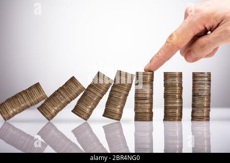 Close-up di un imprenditore la mano proteggere le monete impilate di cadere sulla scrivania riflettente Foto Stock