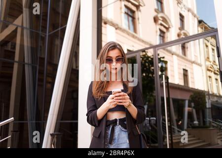carina ragazza giovane in occhiali da sole usa uno smartphone. elegante donna usa uno smartphone per la comunicazione Foto Stock