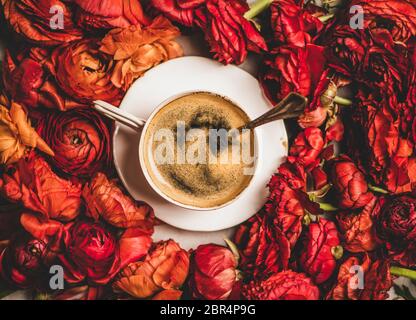 Piatto di caffè espresso nero in tazza di porcellana bianca su fondo fiore rosso, vista dall'alto. Concetto di pausa caffè stagionale in primavera o estate Foto Stock