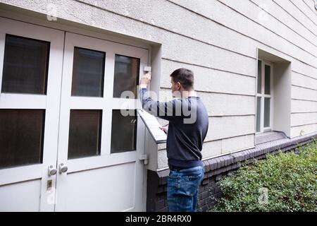 Giovane uomo servizio esaminando porta chiusa all'ingresso Foto Stock