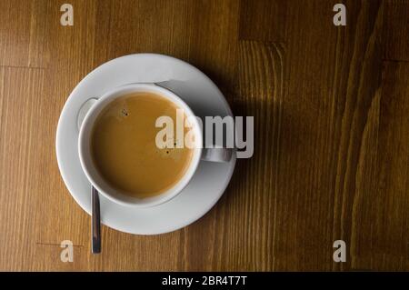 Una tazza di caffè e cucchiaio collocato su un tavolo marrone Foto Stock