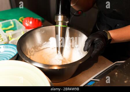 Chef che prepara un mix di formaggi per frittelle al formaggio presso il ristorante. Il frullatore frusta il formaggio di cottage. Preparazione del Cheesecake. Foto Stock