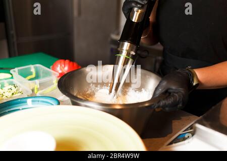 Chef che prepara un mix di formaggi per frittelle al formaggio presso il ristorante. Il frullatore frusta il formaggio di cottage. Preparazione del Cheesecake. Foto Stock