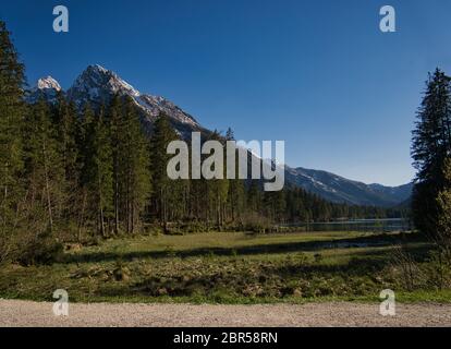 Un sentiero di ghiaia sulla riva del Hintersee a Berchtesgaden con la foresta e la montagna Foto Stock