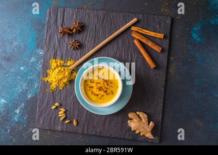 Tè al latte dorato, preparato con curcuma e altre spezie, su sfondo di legno. Bevanda medicinale sana. Disposizione piatta. Foto Stock