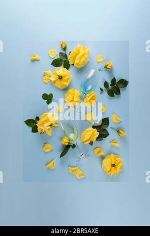 Vista dall'alto del layout creativo composto da due bicchieri da vino con vino bianco e rose gialle e foglie su sfondo blu. Disposizione piatta. Foto Stock