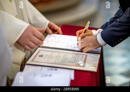 Il govern segni documenti sulla registrazione del matrimonio in presenza del pastore. Coppia giovane segni documenti di matrimonio in chiesa durante il matrimonio Foto Stock