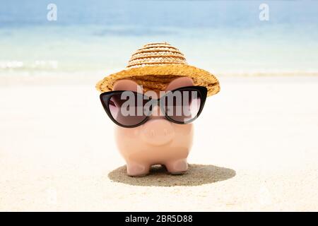 Rosa Piggybank indossando occhiali da sole neri sulla sabbia in spiaggia Foto Stock