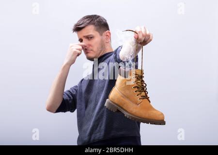 Close-up di un uomo che copre il suo naso tenendo Stinky calzatura contro uno sfondo bianco Foto Stock