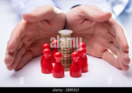 Close-up di mani Proteggere la moneta pila circondato con figure rosse sulla scrivania bianca Foto Stock