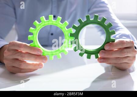 Imprenditore unendo insieme ingranaggi sul tavolo di legno al posto di lavoro Foto Stock
