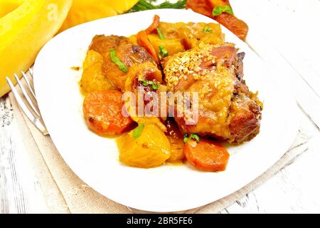 Spezzatino di pollo con zucca, albicocche secche, carote e vino rosso, spolverate con i semi di sesamo in una piastra con un panno da cucina contro lo sfondo di l Foto Stock