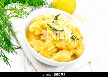 Gnocchi di zucca con salvia, limone, il formaggio e il burro in una ciotola, tovagliolo contro un bianco di legno Foto Stock