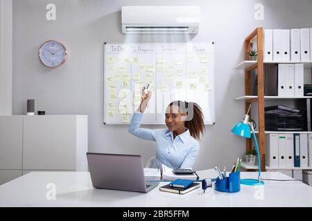 Giovane imprenditrice operante Aria Condizionata con Telecomando in ufficio Foto Stock