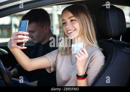 Felice sorridente ragazza prende un selfie con una nuova patente di guida, seduto accanto ad un istruttore Foto Stock