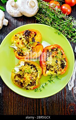 Pepe, farcite con funghi, pomodori, couscous e formaggio in piastra sul tovagliolo, prezzemolo contro lo sfondo della tavola di legno dal di sopra Foto Stock