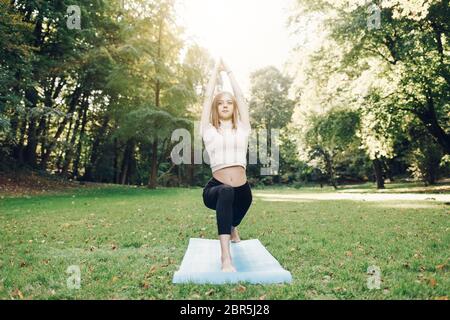 Ragazza che fa esercizi di yoga nel tappetino sportivo al parco pubblico Foto Stock