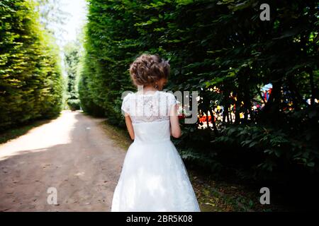 La sposa in un abito da sposa bianco tiene un bouquet sullo sfondo di un parco verde Foto Stock
