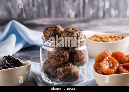 Palle energetiche di frutta secca e noci in un vaso di vetro, accanto agli ingredienti per cucinare albicocche secche, prugne, mandorle. Il concetto di vega sano Foto Stock