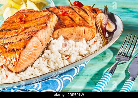 Gourmet di salmone fresco bistecche condite con peperoncino e alla griglia su un barbecue servito su un letto di riso salato con cipolle arrosto Foto Stock