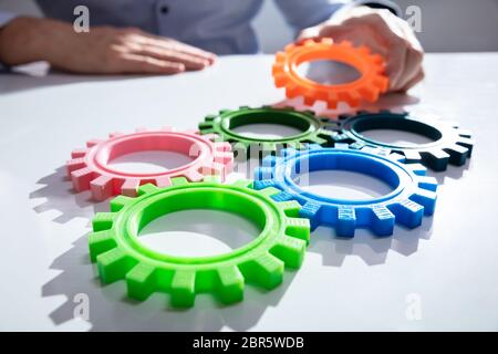 Imprenditore unendo insieme ingranaggi sul tavolo di legno al posto di lavoro Foto Stock