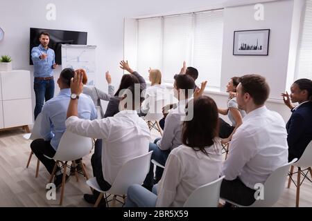 Presentatore maschio di porre domande al suo collega alzando le mani durante il seminario in ufficio Foto Stock