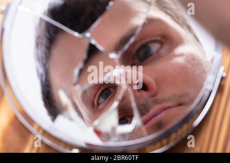 Close-up del giovane uomo che guarda il suo volto in uno specchio rotto Foto Stock