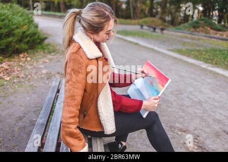 Artista ragazza dipinge una foto su tela proprio nel parco su una panchina. La donna disegna un'immagine che la tiene nelle mani Foto Stock