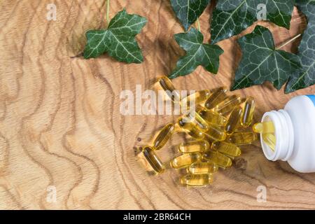 Capsule di olio di pesce gelatinose trasparenti fuoriuscite dalla bottiglia su fondo di legno. Acidi grassi polinsaturi Omega-3-essenziali. Co Foto Stock