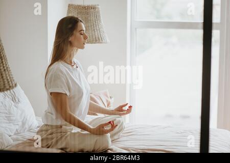 Bella giovane donna che pratica la meditazione sul letto a casa. Foto Stock