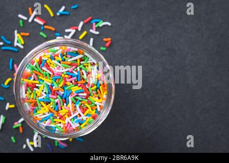 Lo zucchero colorato si sprigola in un vaso di vetro, fotografato in alto sull'ardesia (fuoco selettivo, fuoco sugli spruzzi nel vaso) Foto Stock