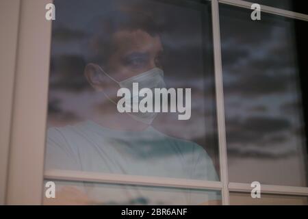 Uomo triste in una maschera medica guardare la finestra. 4K Foto Stock