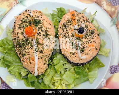 Metà di Avocado riempita con una crema di salmone, riccamente decorate con erbe e caviale su un letto di lattuga, il tutto su un piatto rotondo in vista superiore e close-up. Foto Stock