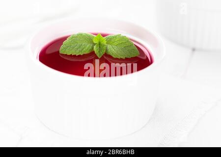 Gelatina rossa o jella nella ciotola bianco guarnito con foglie di menta (messa a fuoco selettiva, concentrarsi sulle punte delle grandi foglie di menta) Foto Stock