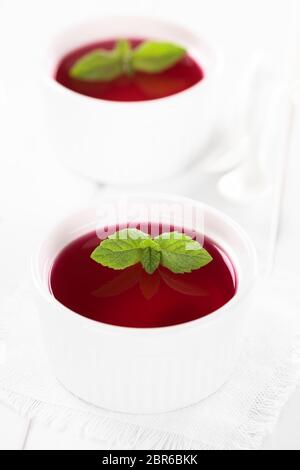 Gelatina rossa o jella in bianco ciotole guarnite con foglie di menta (messa a fuoco selettiva, concentrarsi sulle punte delle foglie di menta nel primo recipiente) Foto Stock