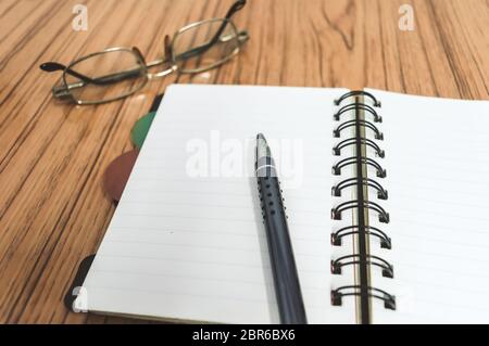 Scrivania con il notebook aperto con pagine vuote, occhiali e una penna. Business ancora il concetto di vita con office roba sulla tabella. Istruzione, lavoro e planni Foto Stock