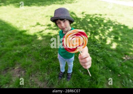 Ragazzo gioioso che tiene un lecca nelle mani. Distorsione dell'obiettivo grandangolare. Mettere a fuoco il primo piano. Foto Stock