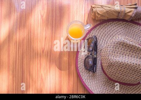 Pronto a viaggiare. Vista dall'alto sullo sfondo della spiaggia di accessori essenziali per il viaggio estivo delle donne in un tavolo di legno. Occhiali da sole, ombrello, cappello di paglia e. Foto Stock