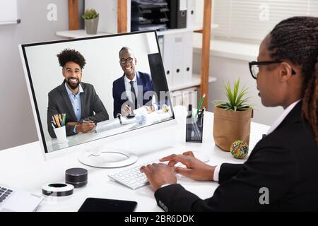 Vista laterale di una giovane imprenditrice la videoconferenza con i suoi colleghi sul computer Foto Stock