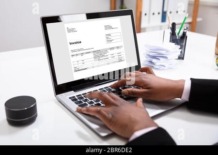 Close-up di una imprenditrice la mano della fattura di controllo su Laptop vicino a fatture su scrivania Foto Stock