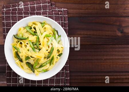 Freschi Fatti in casa piatto di pasta di fettuccine o tagliatelle, asparagi verdi, aglio e il succo di limone in un recipiente, il pepe nero macinato sulla parte superiore, fotografato Foto Stock