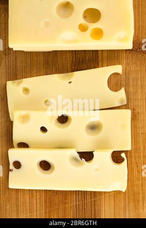 Pezzo e fette di Emmental, Formaggi Emmental o formaggio Groviera, fotografato overhead su legno (messa a fuoco selettiva, concentrarsi sulle fette) Foto Stock