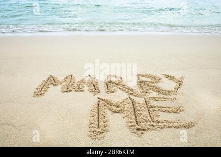 Sposarsi Me Scritta sulla sabbia con impronte vicino al mare in spiaggia Foto Stock