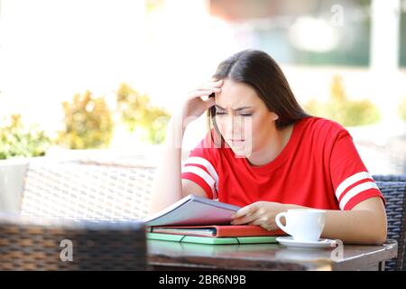 Preoccupato studente cercando di capire la lezione note di lettura di seduta in una caffetteria e terrazza Foto Stock