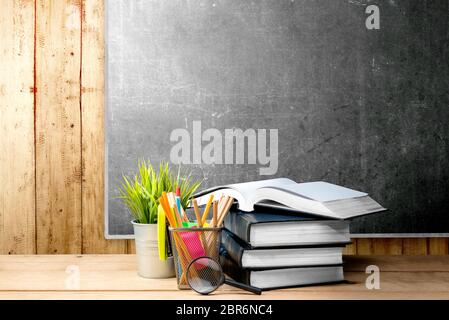 Pila di libri con pianta in vaso e matite in contenitore a cestello con lente di ingrandimento sul tavolo di legno con blackboard sfondo. Si torna a scuola c Foto Stock