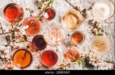 Varie sfumature di vino rosato. Piatto-lay di vino rosa in diversi colori in bicchieri e fiori primavera fiore su sfondo di marmo, vista dall'alto. Cenere di vino Foto Stock