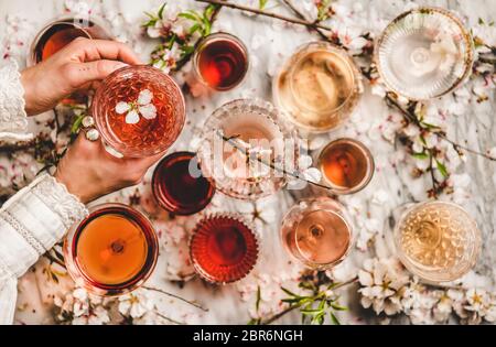 Le donne passano le sfumature offerenti del vino rosa in bicchieri e fiori di primavera fioriti su sfondo bianco, vista dall'alto. Enoteca, bar, degustazione vini, w Foto Stock